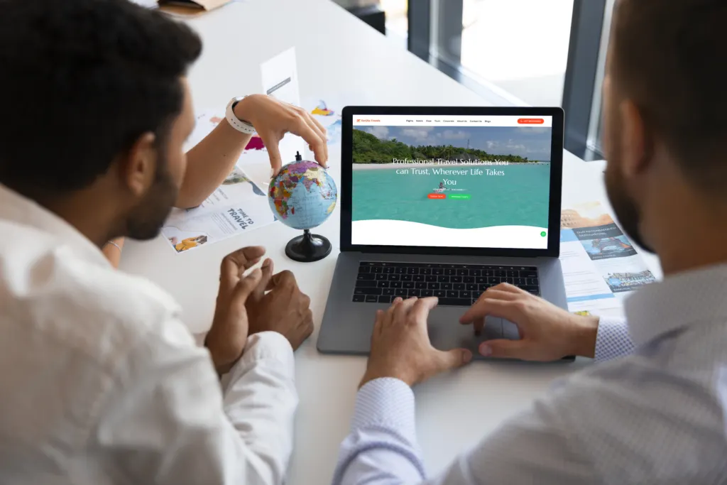 Two colleagues planning a trip on a laptop with a small globe on the desk
