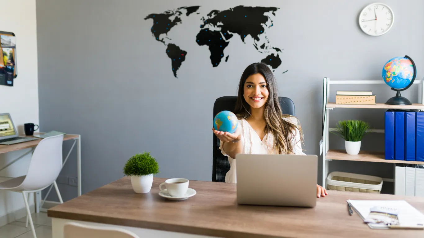 Travel consultant smiling at her desk holding a small globe