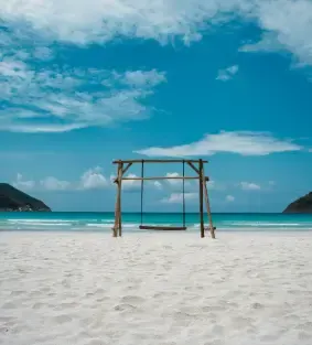 Wooden swing on a white sand beach under a blue sky