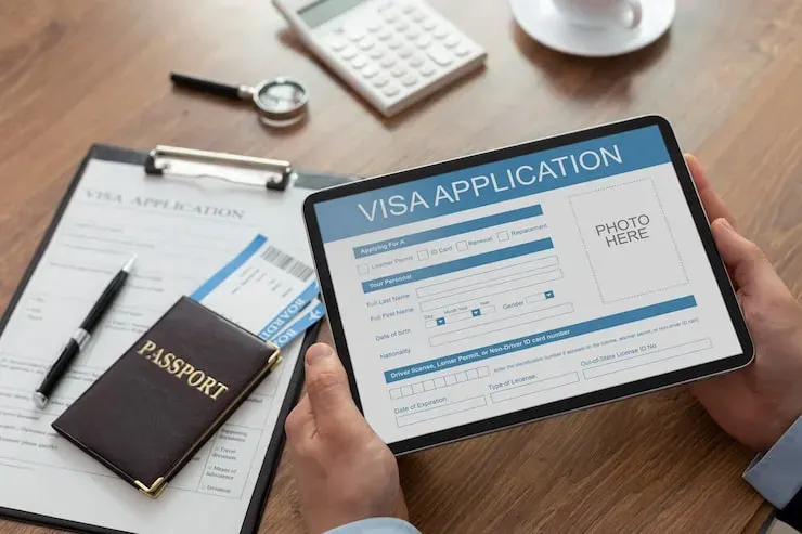 Hands holding a tablet showing a visa application form beside a passport