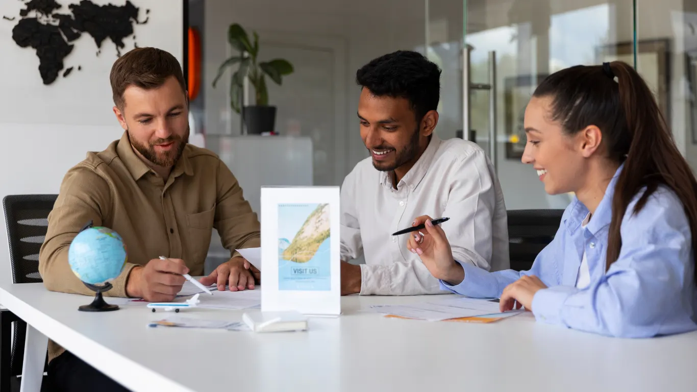 Three colleagues at a desk discussing travel documents beside a small globe